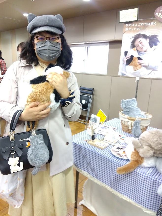 CocoMeowのブース前で三毛ちゃんを抱えて立つ北村由衣