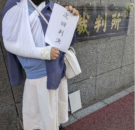 東京地裁前で「次回判決」と書かれた紙を掲げる北村由衣