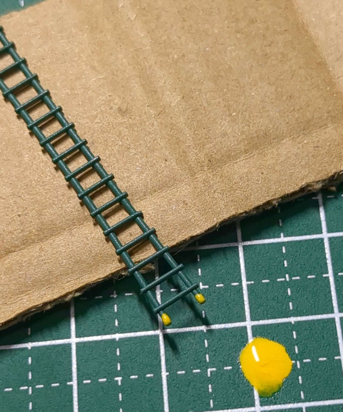 緑色で成型された梯子の先端を黄色で塗っている作業風景。作業用マットに塗料が垂れてしまっている
