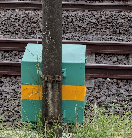 西武の鉄道沿いに設置されている電話箱の写真。薄い緑色の箱に黄色の帯がペイントされている