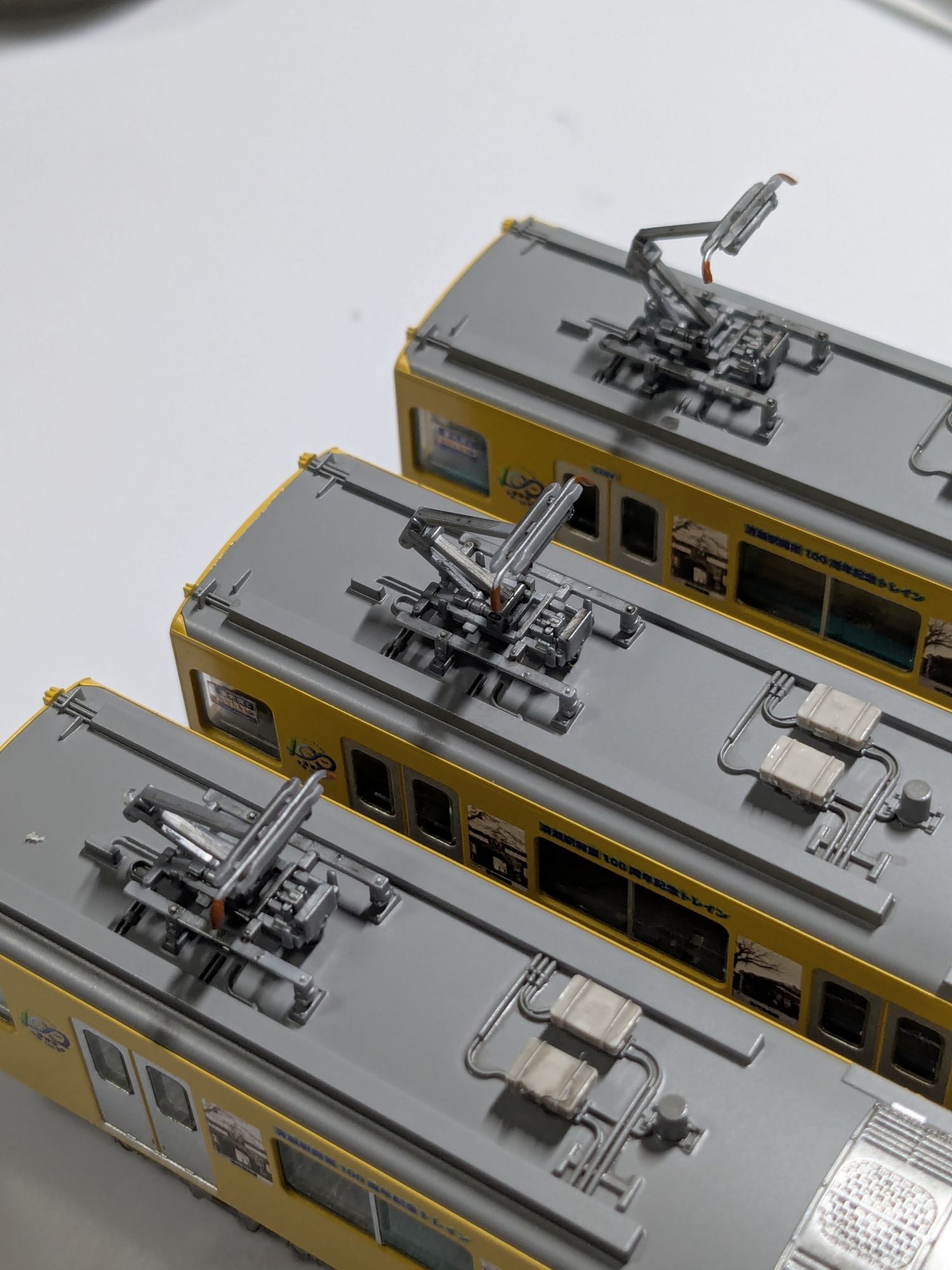 パンタグラフの先端を橙色に塗装した模型が3両並べられている写真