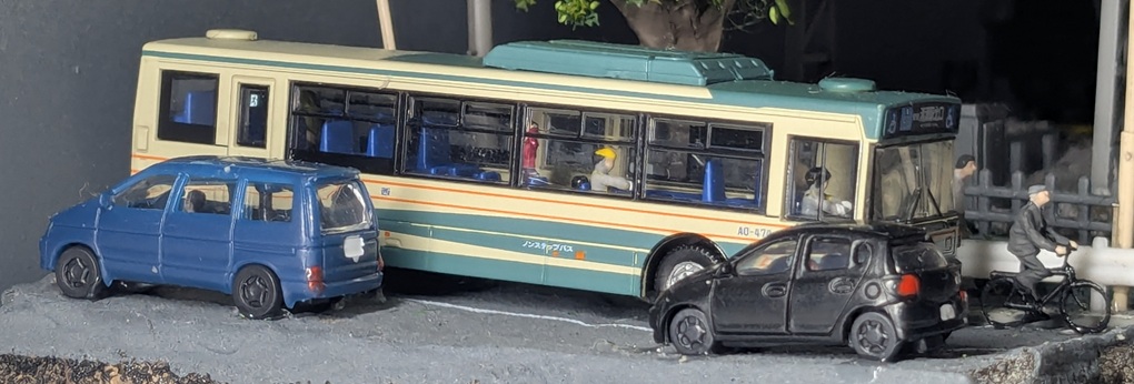 完成状態の道路部分。手前車線に乗用車が二台、奥の車線に乗客を乗せたバスと自転車が走っている